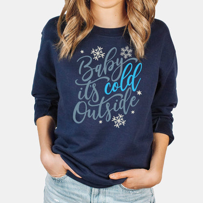 A woman wearing a navy drop-shoulder Tultex sweatshirt featuring snowflakes and the words baby it's cold outside.