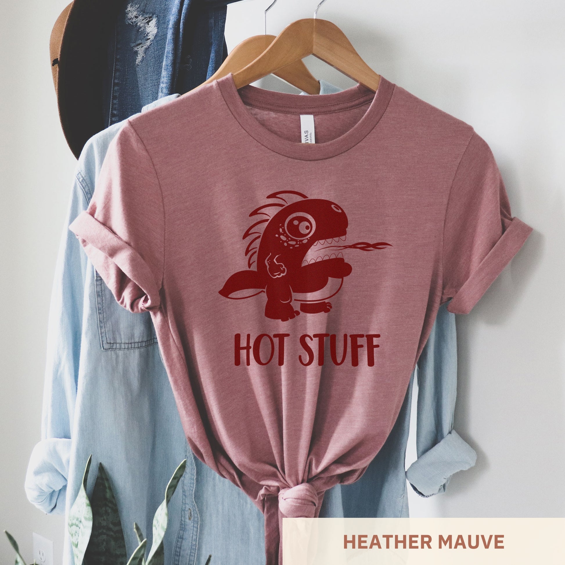 A hanging heather mauve Bella Canvas t-shirt wearing a cute cartoon monster that is belching fire with the words hot stuff.
