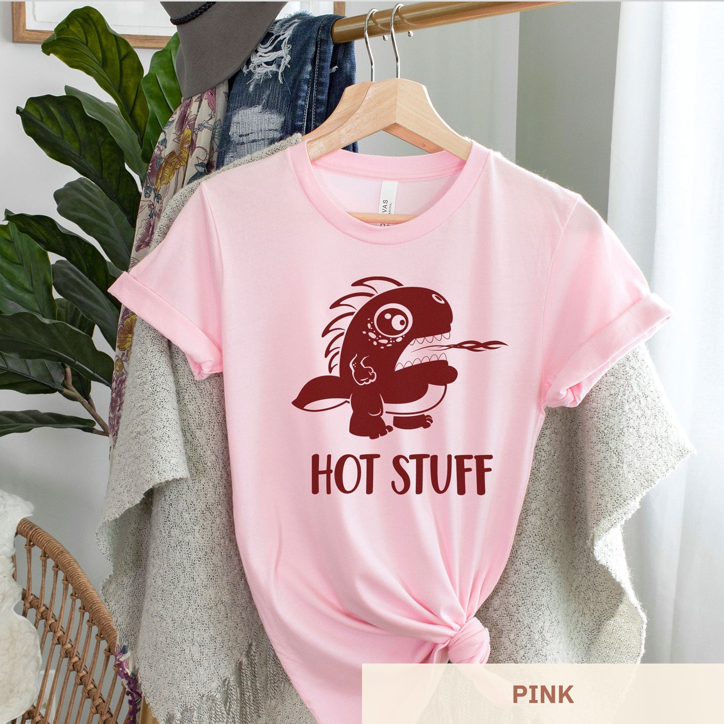 A hanging pink Bella Canvas t-shirt wearing a cute cartoon monster that is belching fire with the words hot stuff.