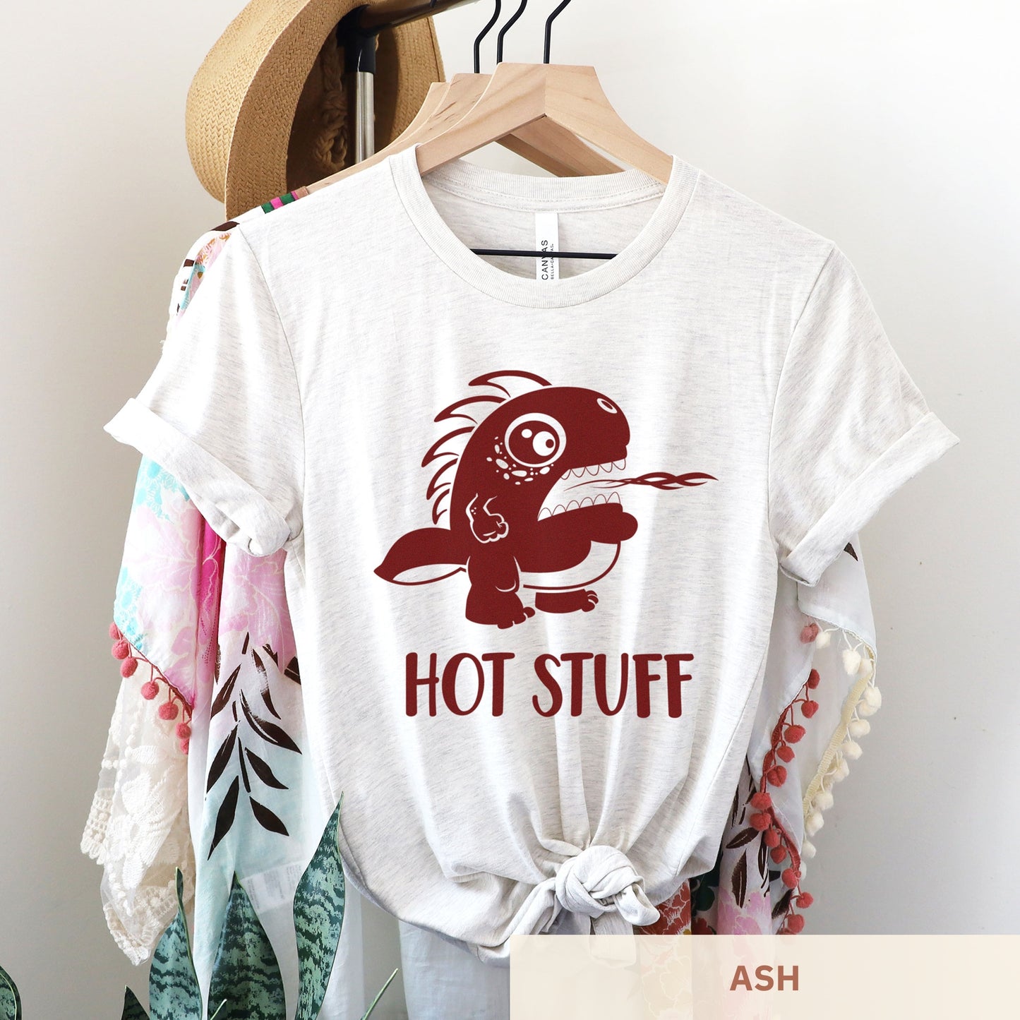 A hanging ash Bella Canvas t-shirt wearing a cute cartoon monster that is belching fire with the words hot stuff.
