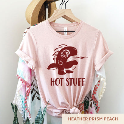 A hanging heather prism peach Bella Canvas t-shirt wearing a cute cartoon monster that is belching fire with the words hot stuff.