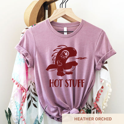 A hanging heather orchid Bella Canvas t-shirt wearing a cute cartoon monster that is belching fire with the words hot stuff.