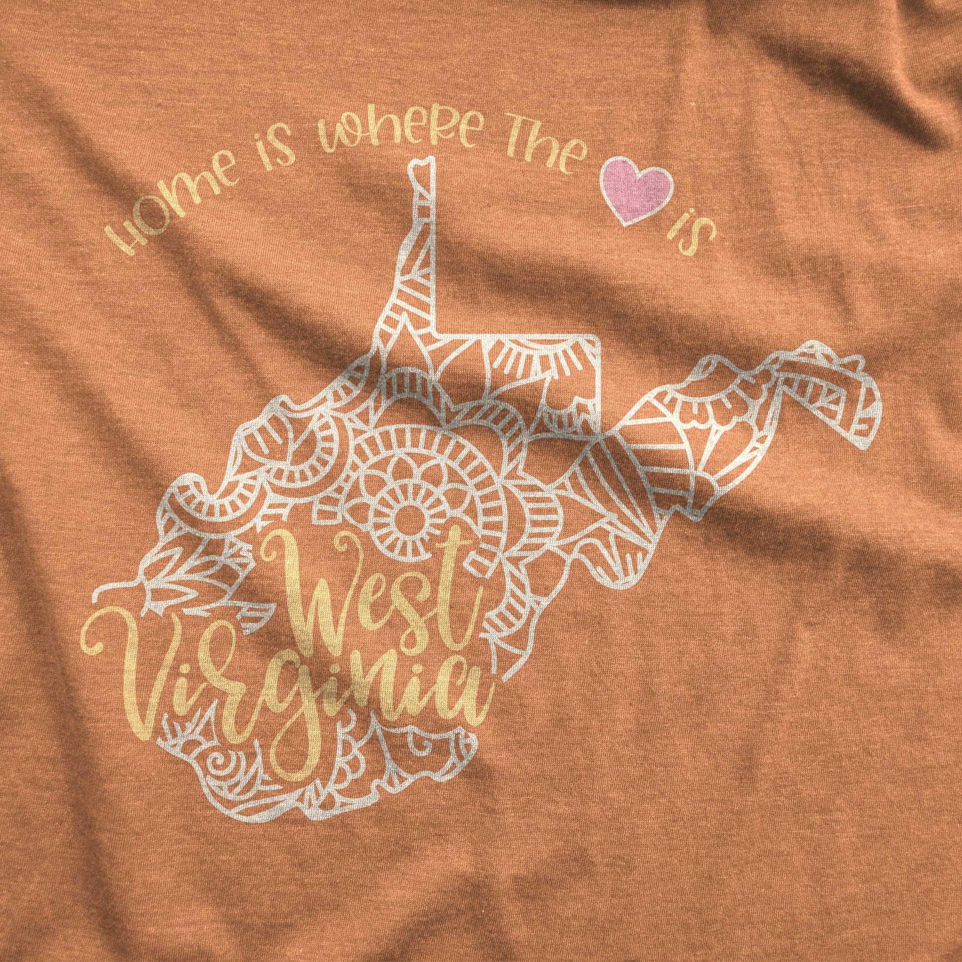 A heather autumn Bella Canvas swatch featuring a mandala in the shape of West Virginia with the words home is where the heart is.