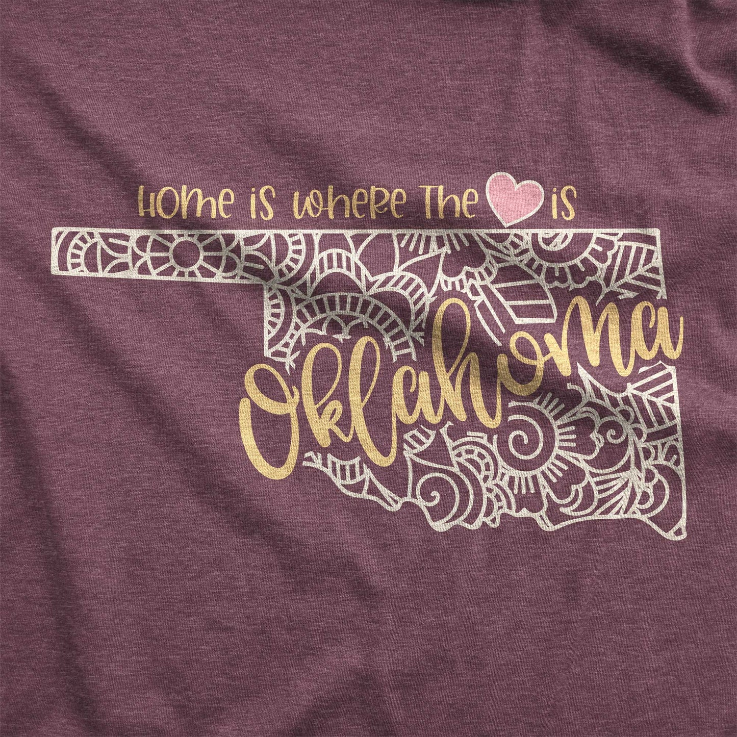 A heather maroon Bella Canvas switch featuring a mandala in the shape of Oklahoma with the words home is where the heart is.