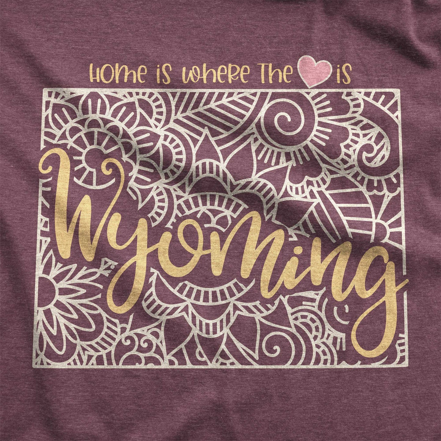 A heather maroon Bella Canvas swatch featuring a mandala in the shape of Wyoming with the words home is where the heart is.